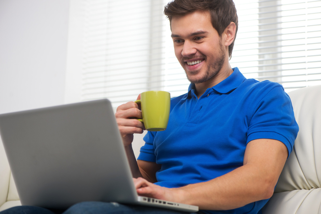 Young man happy on sofa with laptop.